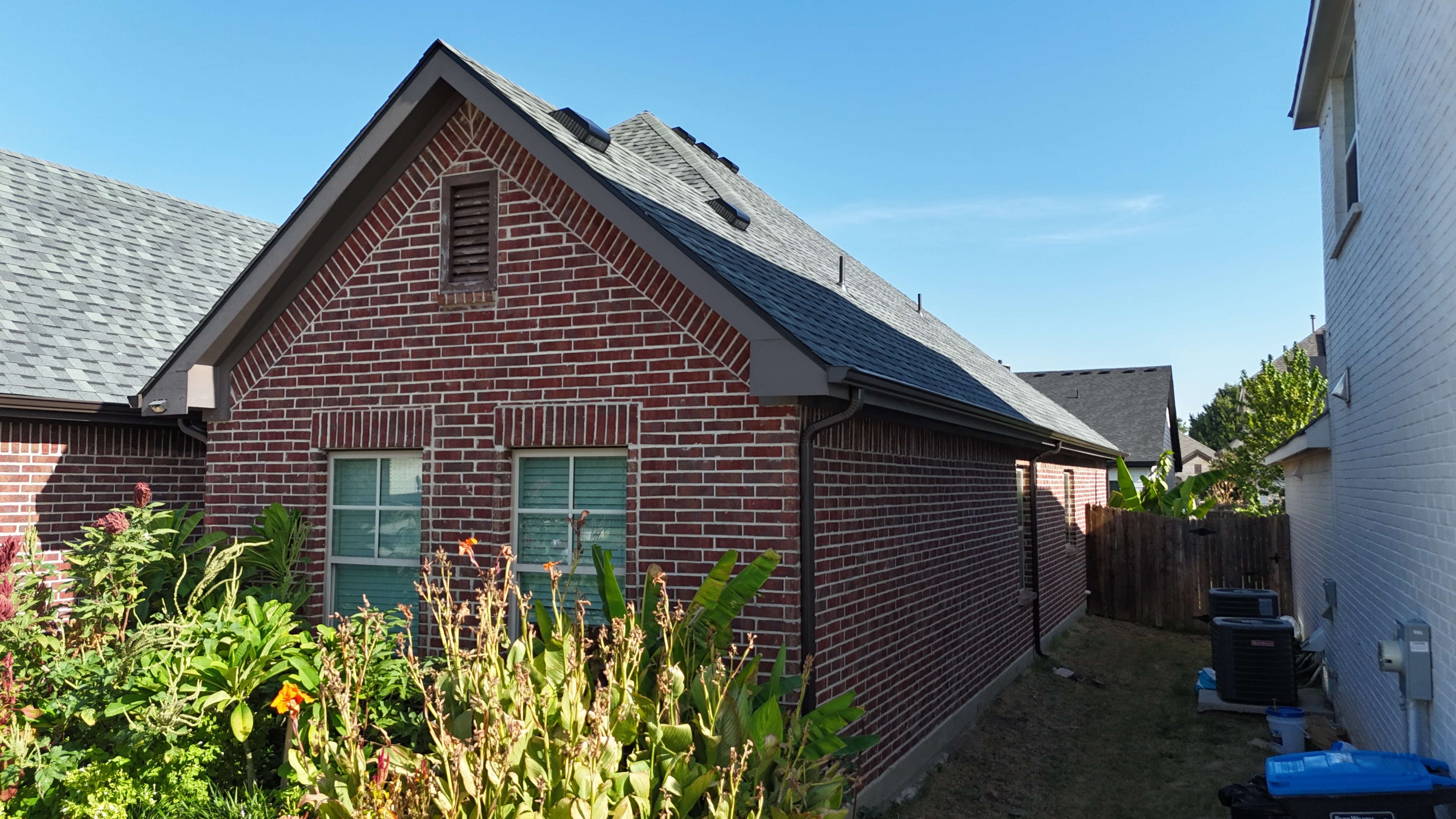 Ground-level side view of completed gray roof on red brick home with landscaping