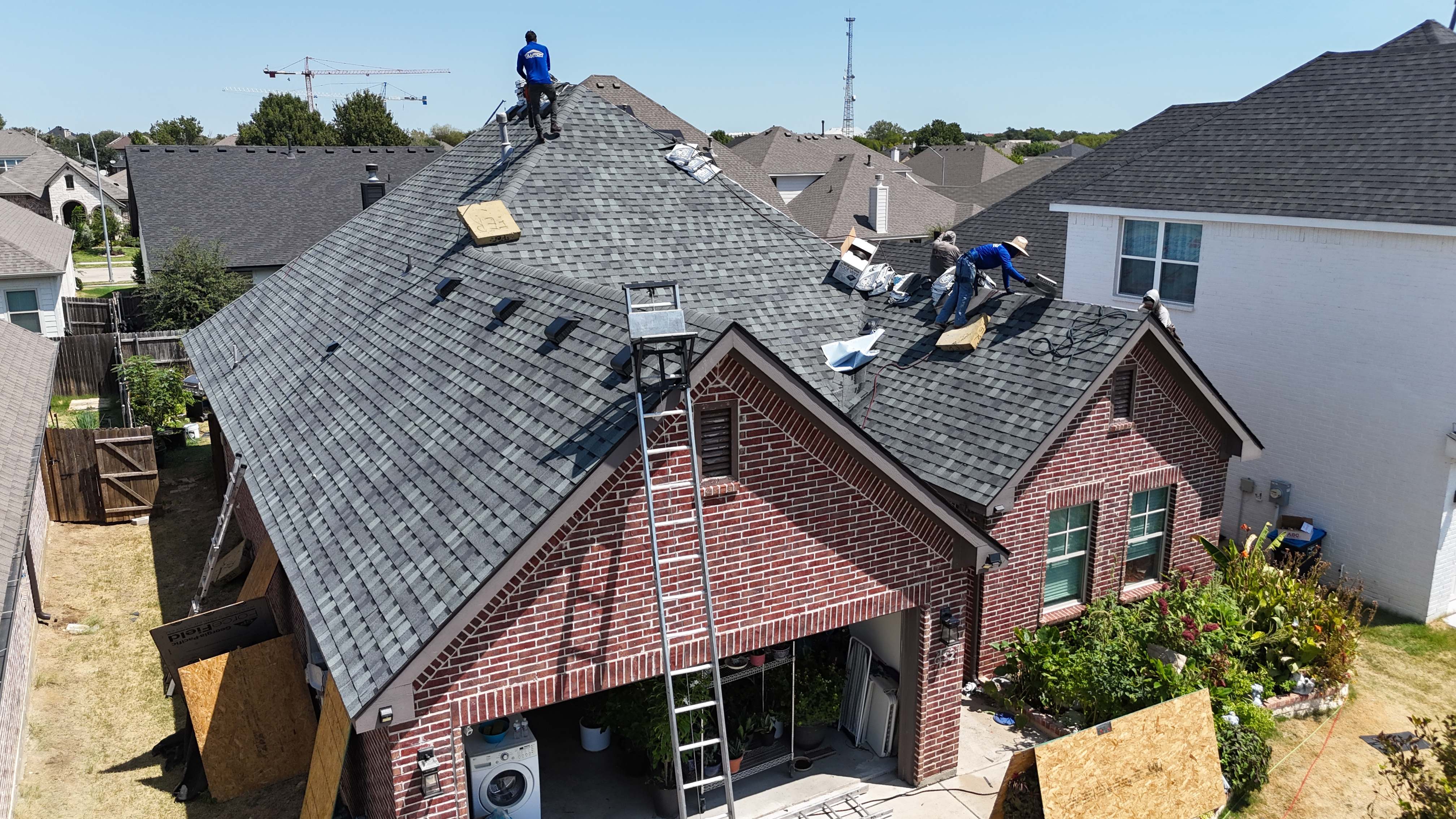 Roofing crew installing shingles on red brick Texas home