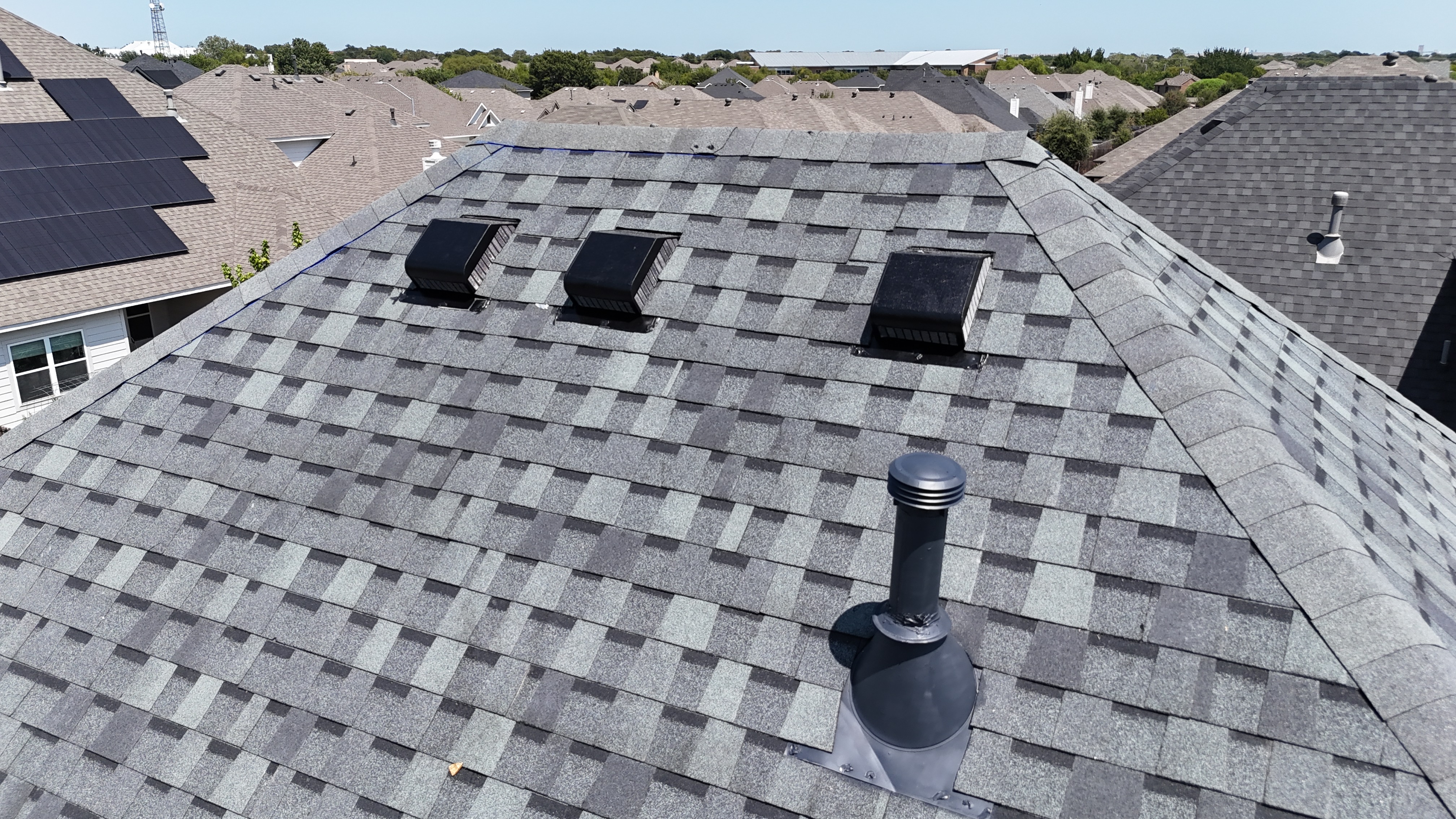 Close-up of ridge vents and pipe boot on completed gray shingle roof