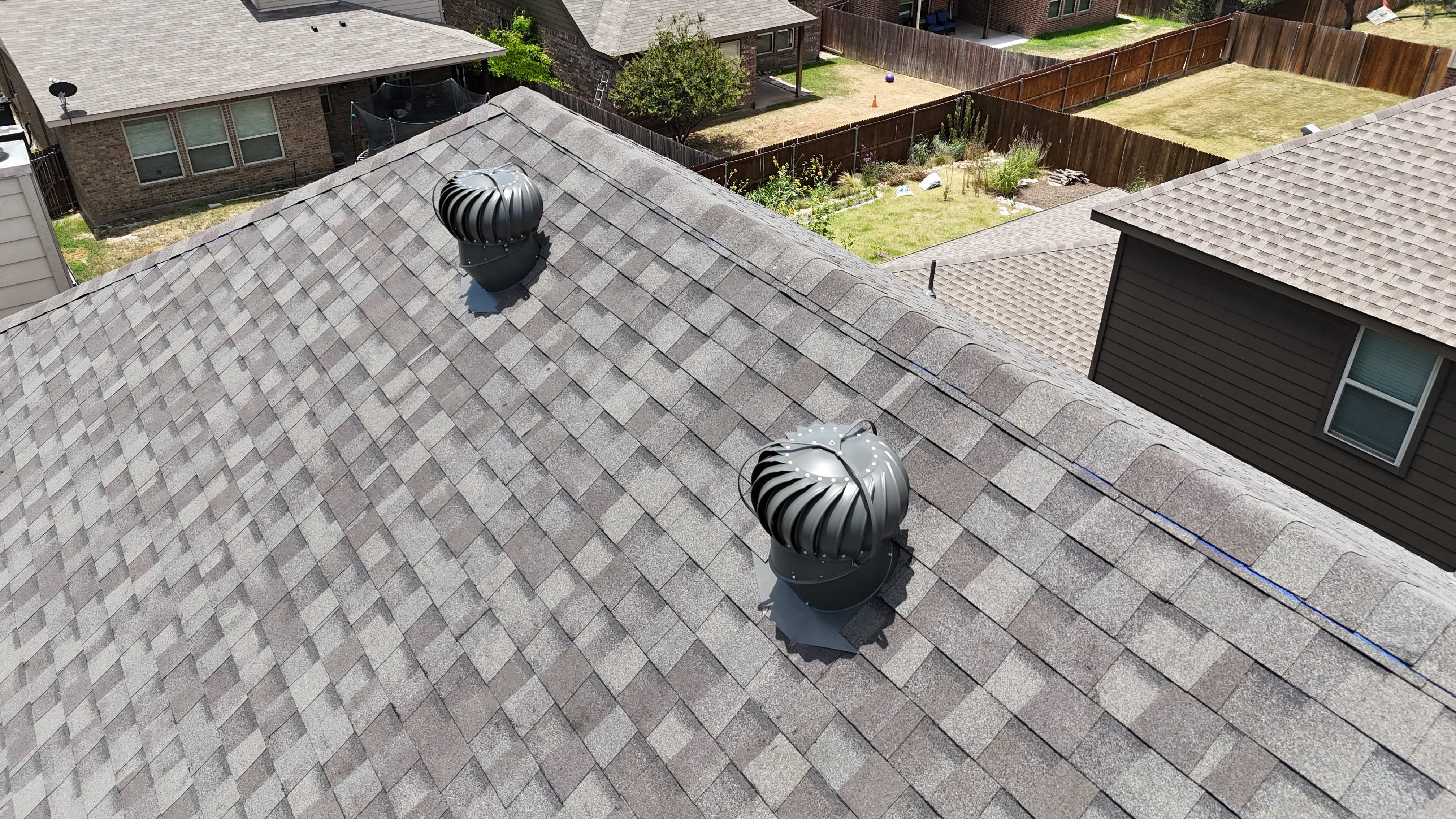 Close-up aerial of two black turbine vents on completed brown shingle roof