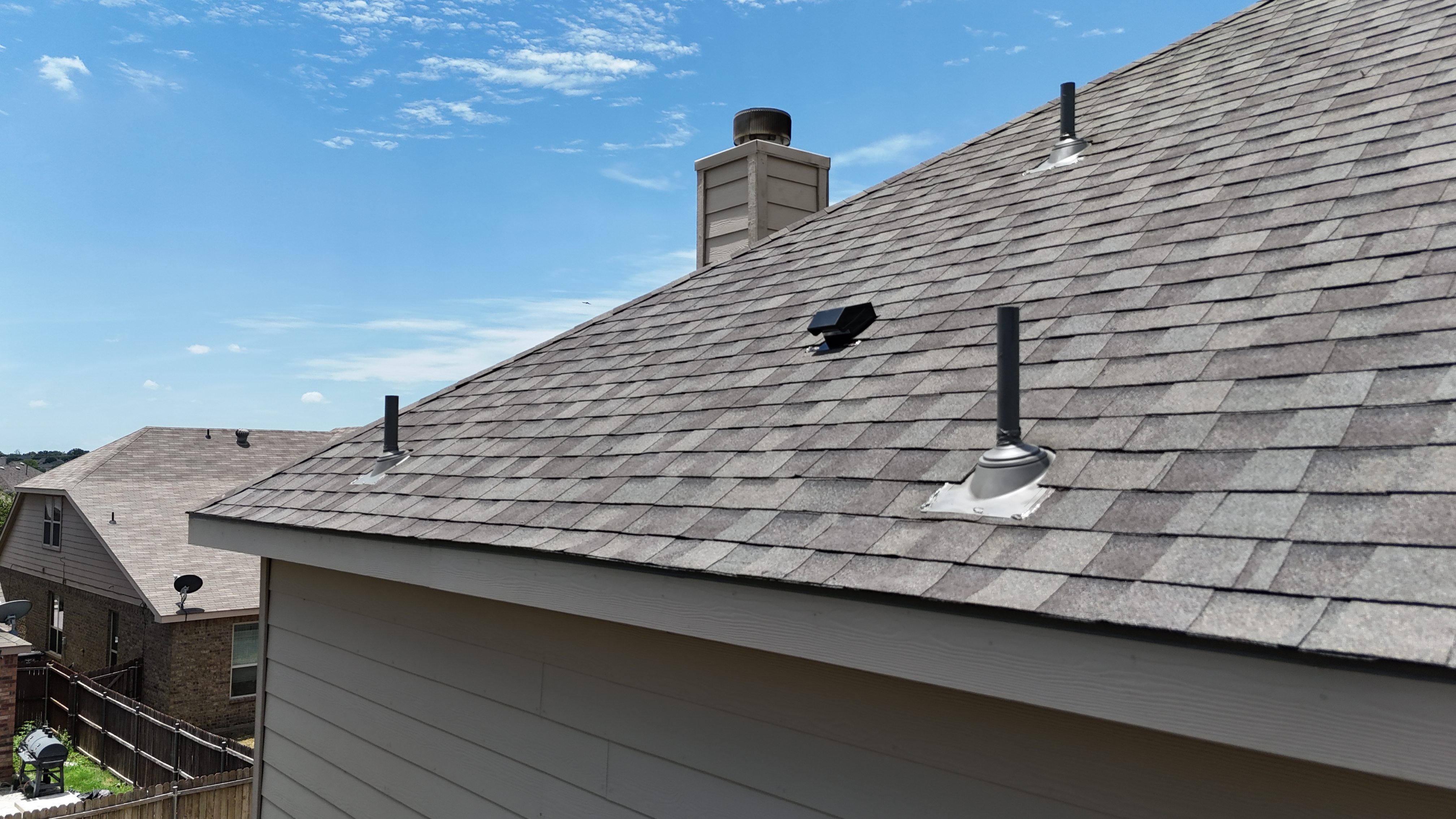 Brown shingle roof detail with chimney, box vent, and pipe vents against blue sky
