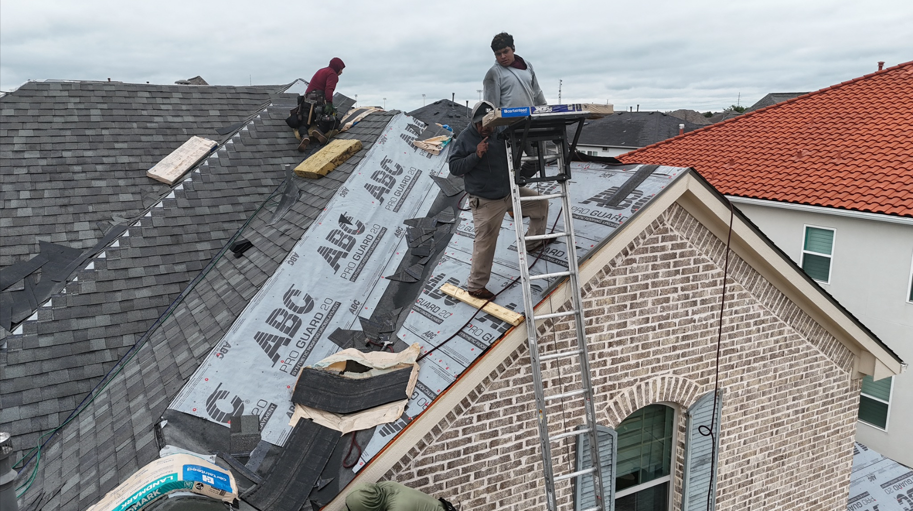 Workers carrying shingle bundles up ladder to roof