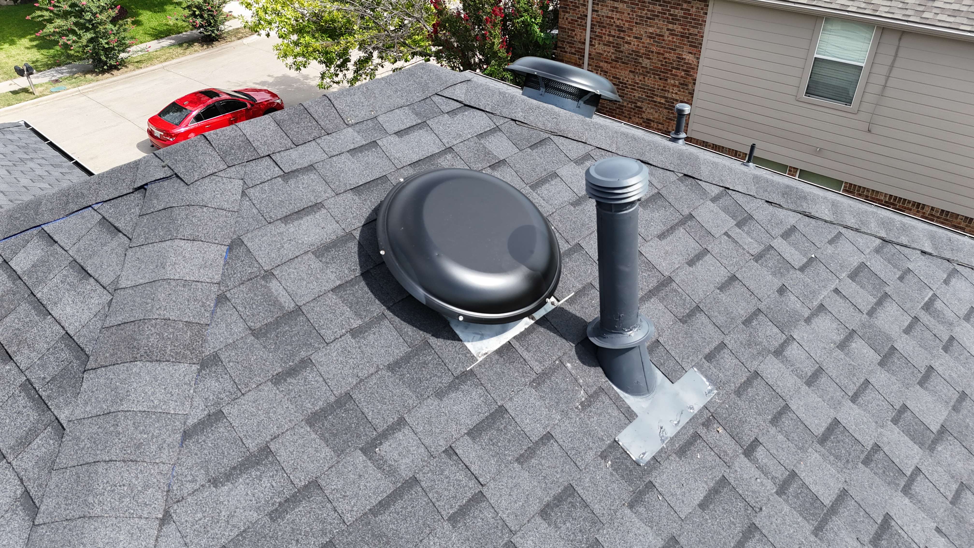 Close-up of attic dome vent and plumbing stack on completed charcoal shingle roof