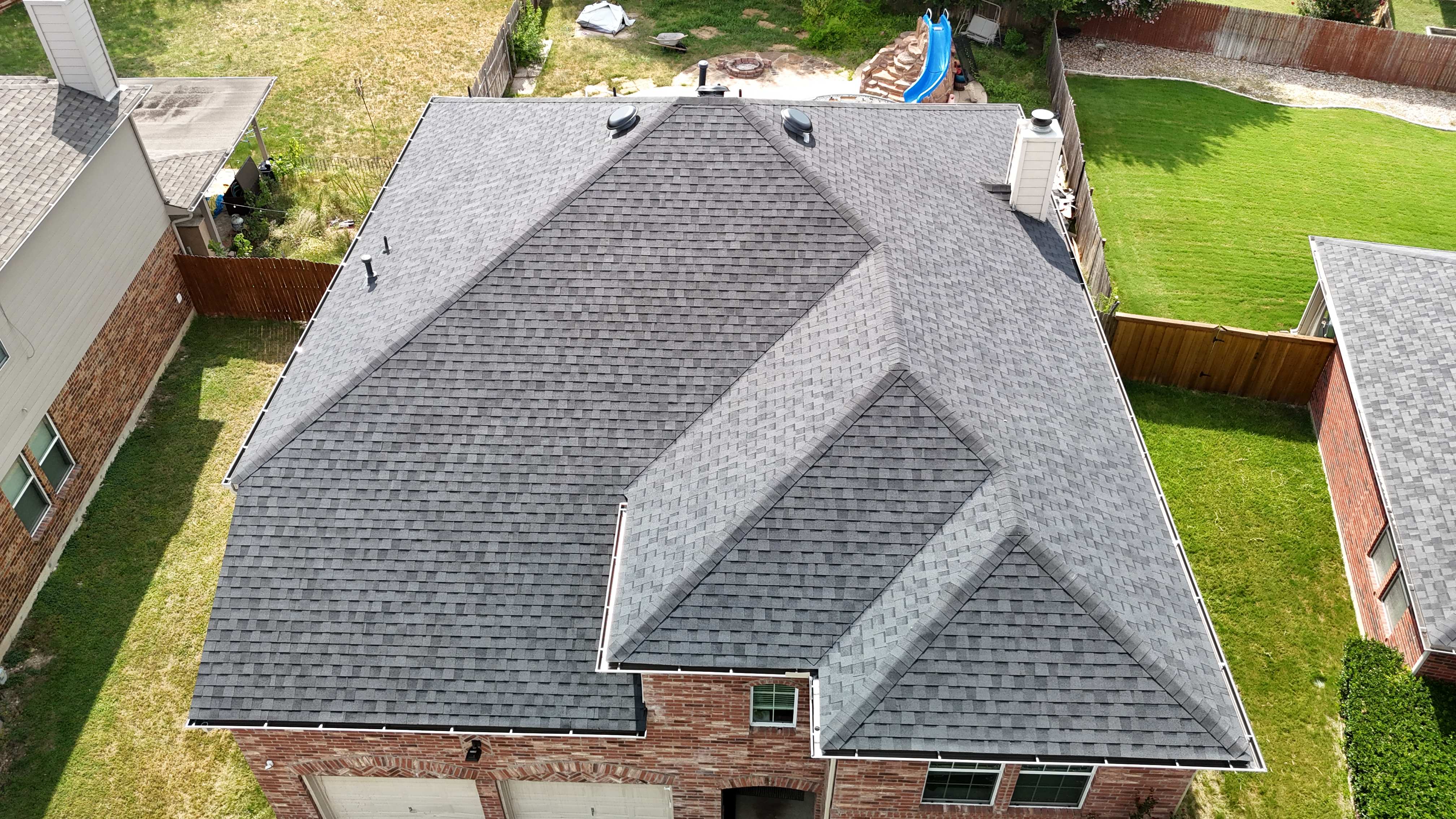 Aerial view of completed charcoal shingle roof on brick home with backyard slide