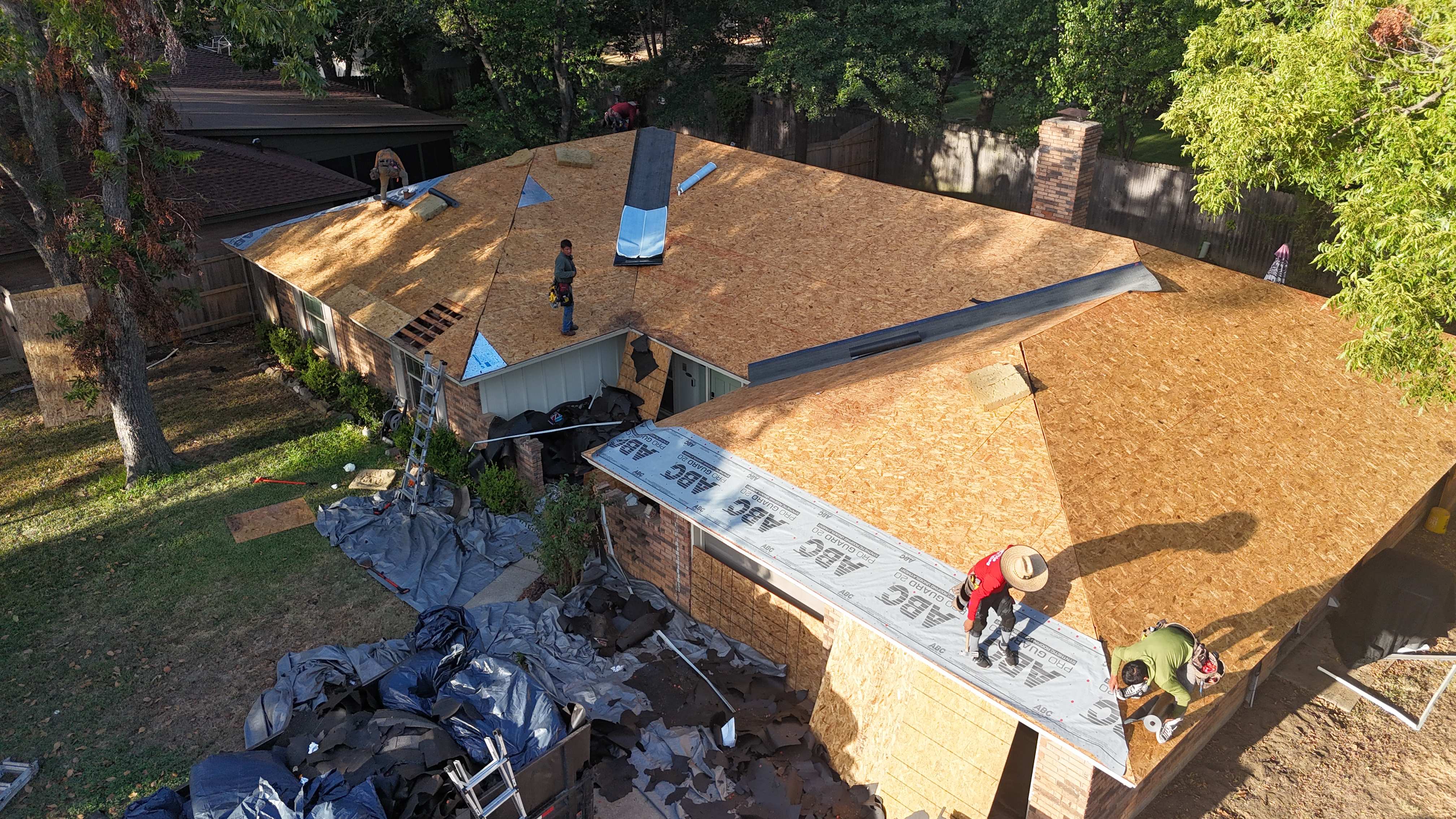 Aerial view of new OSB roof decking with crew laying underlayment