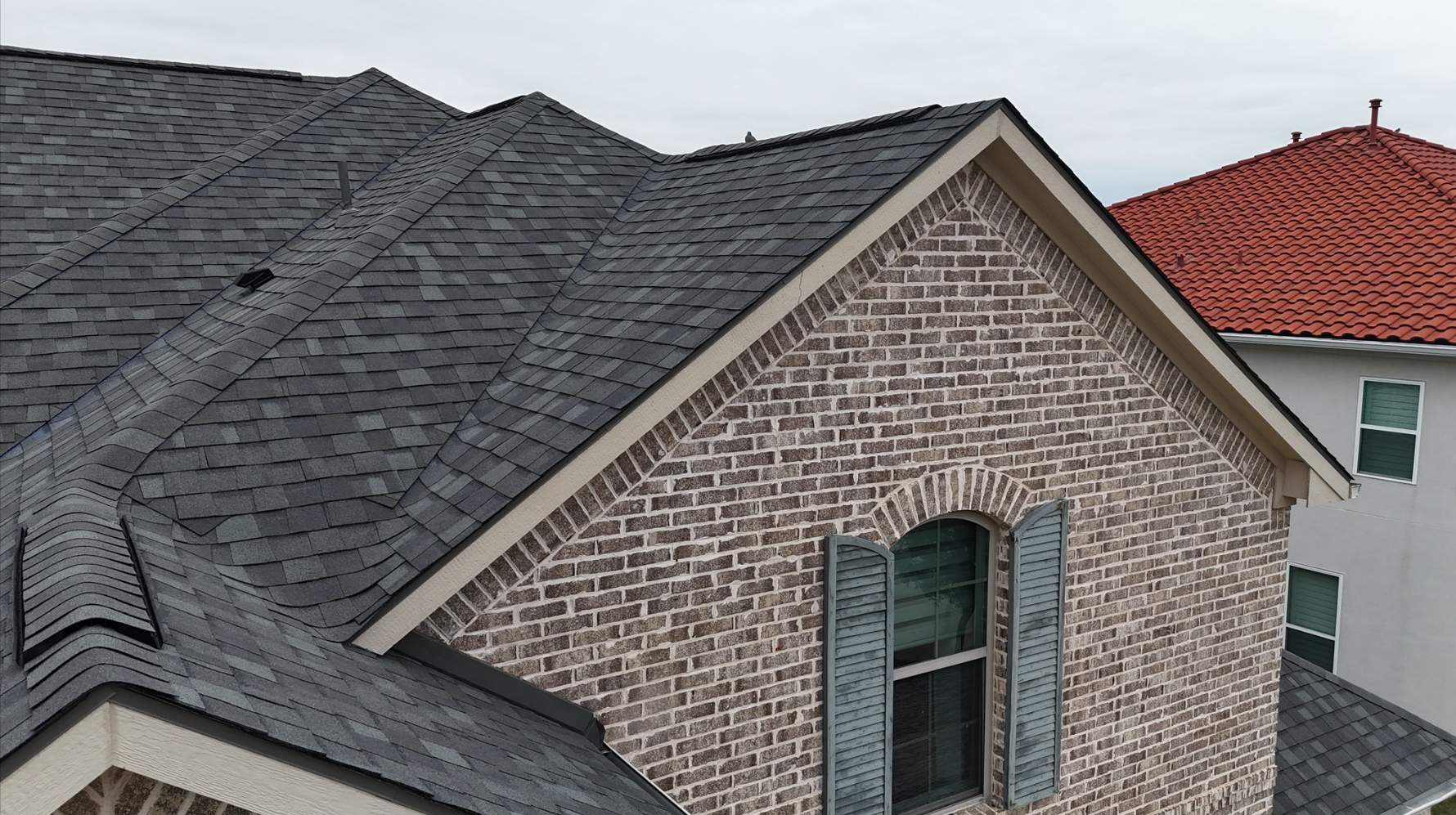 Close-up of completed gray shingle roof on brick home