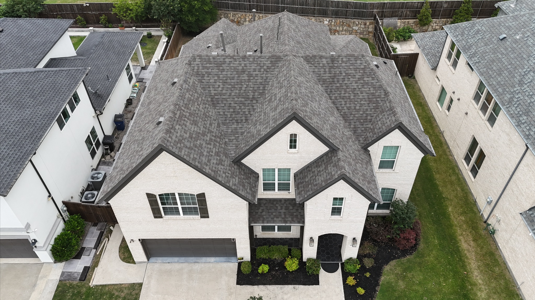 Aerial front view of completed gray roof on white brick two-story home