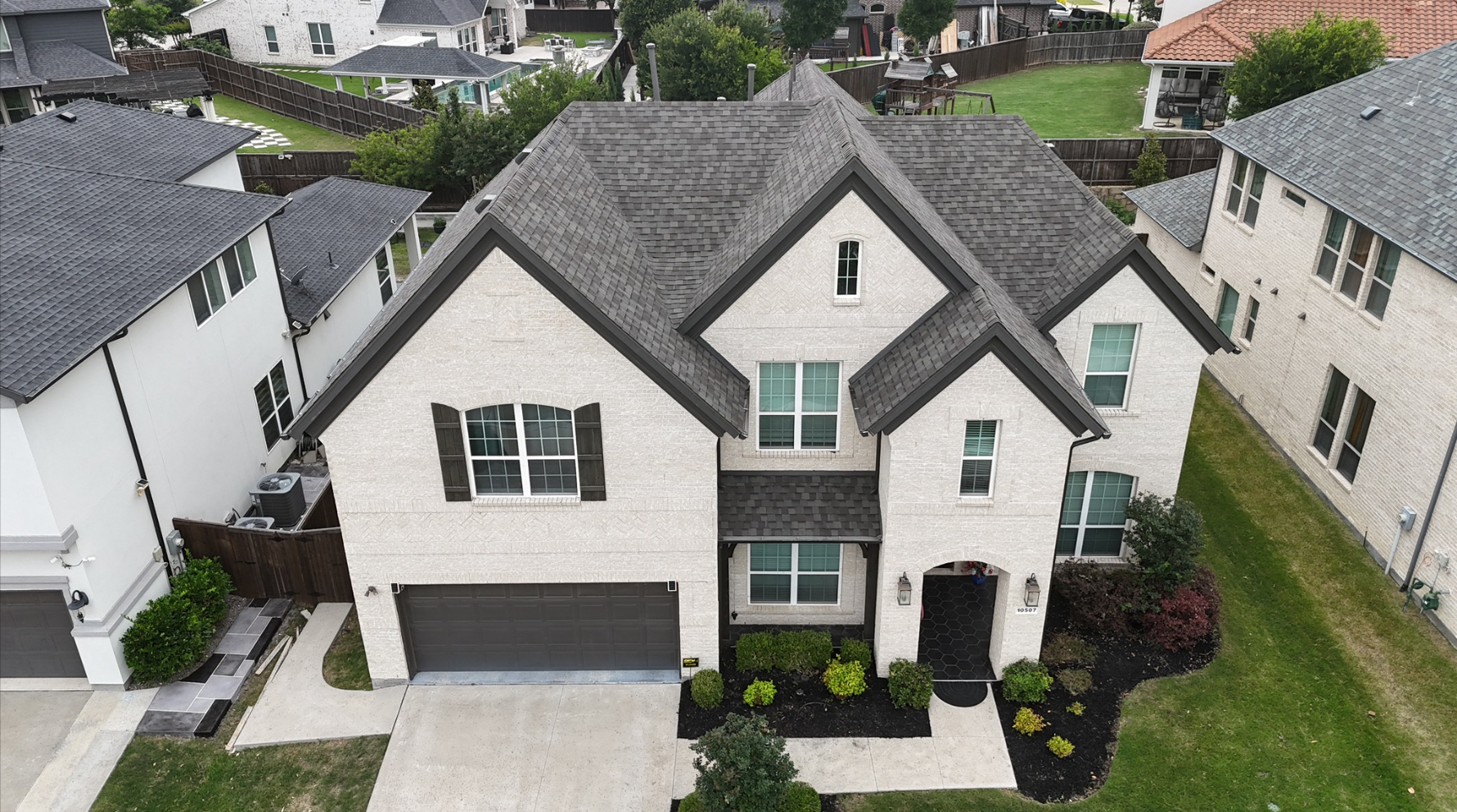 Beautiful completed charcoal roof on luxury white brick home with landscaping