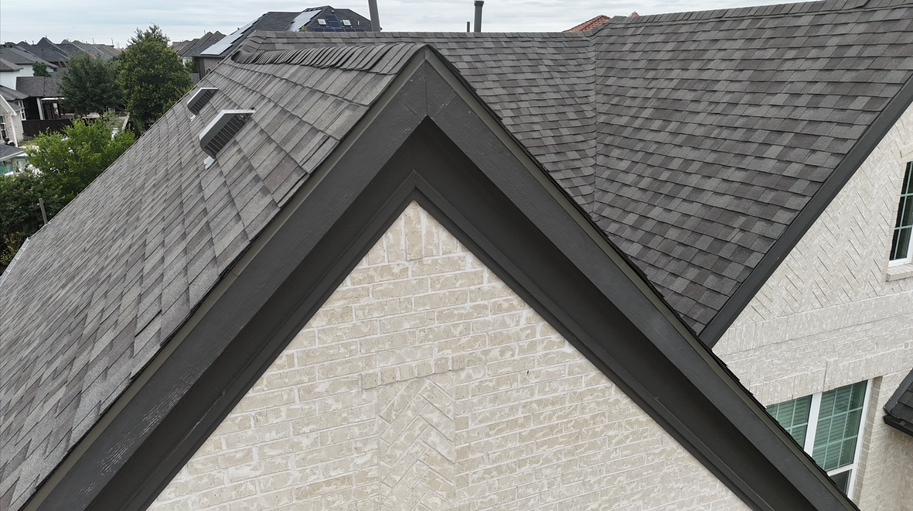 Close-up detail of roof peak showing clean shingle lines on white brick home