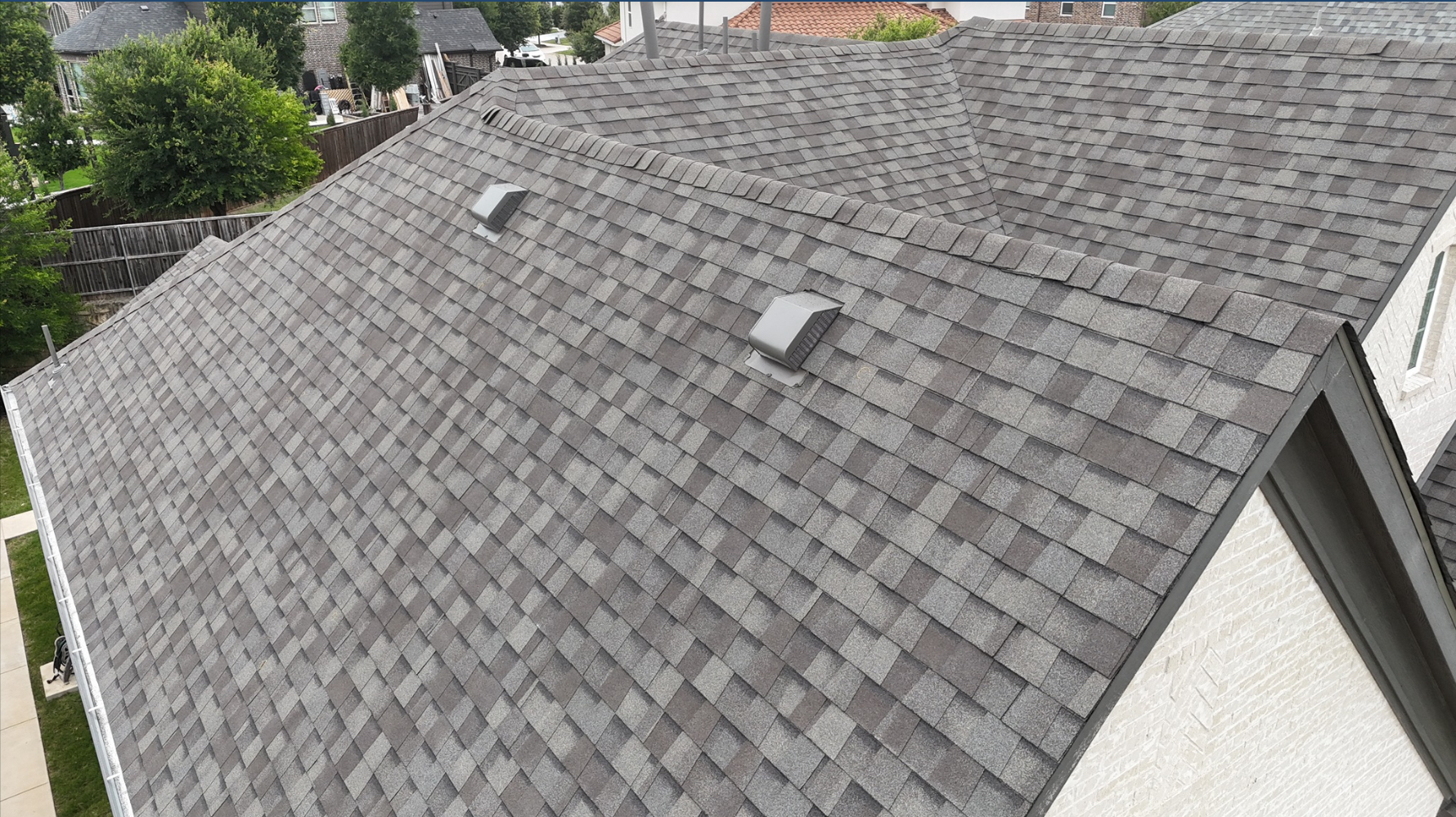 Aerial side view of completed gray roof with vents on white brick home