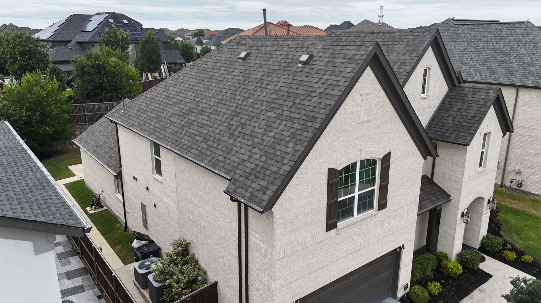 Completed dark charcoal shingle roof on white brick home - side view