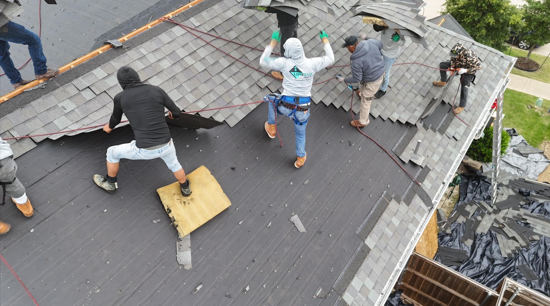 Roofing crew installing shingles with safety equipment