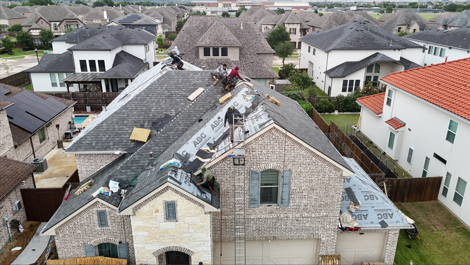 Aerial view of crew installing shingles on two-story Texas home
