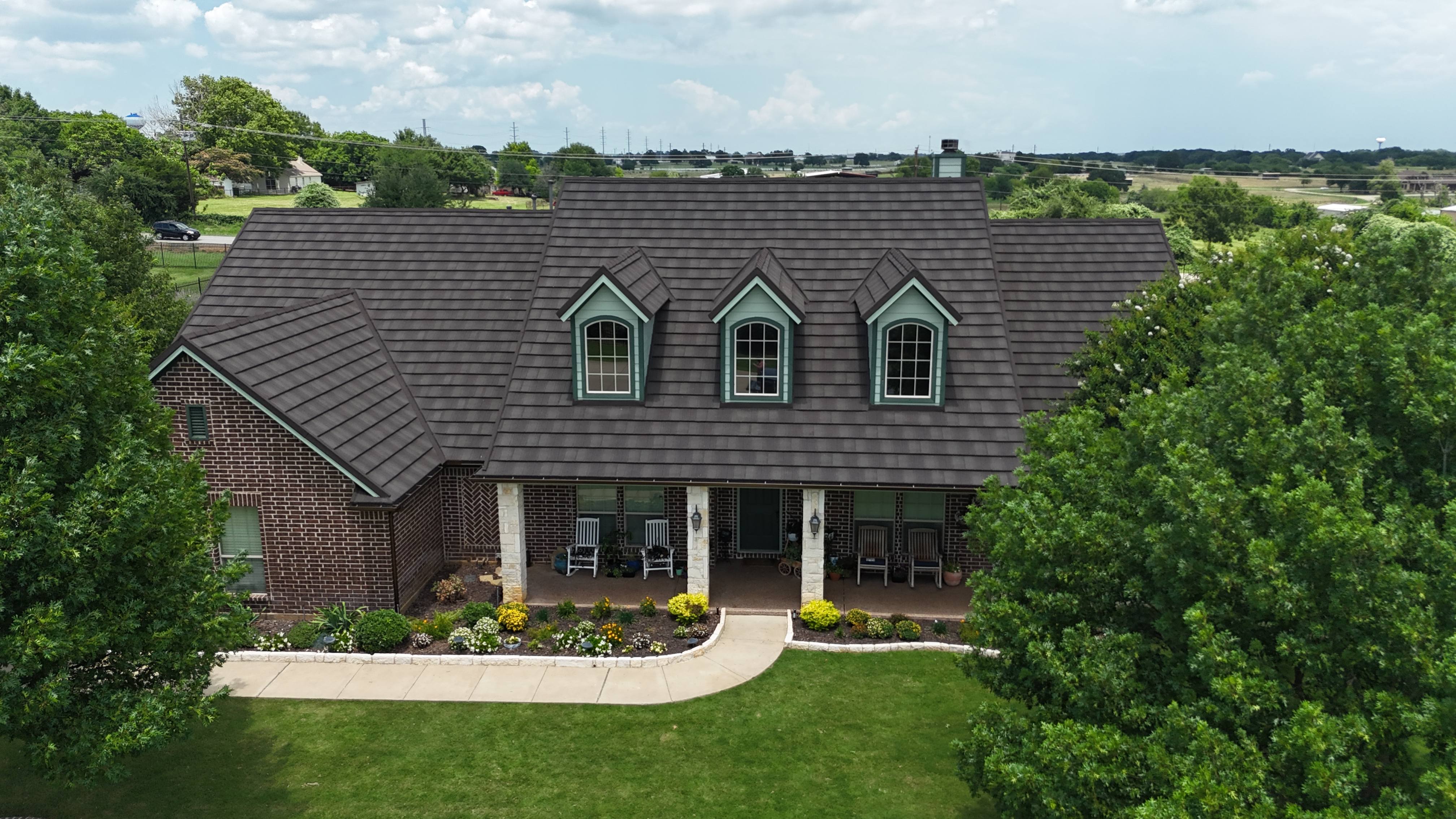 Front elevation of brick home with brown stone coated steel roof and dormer windows