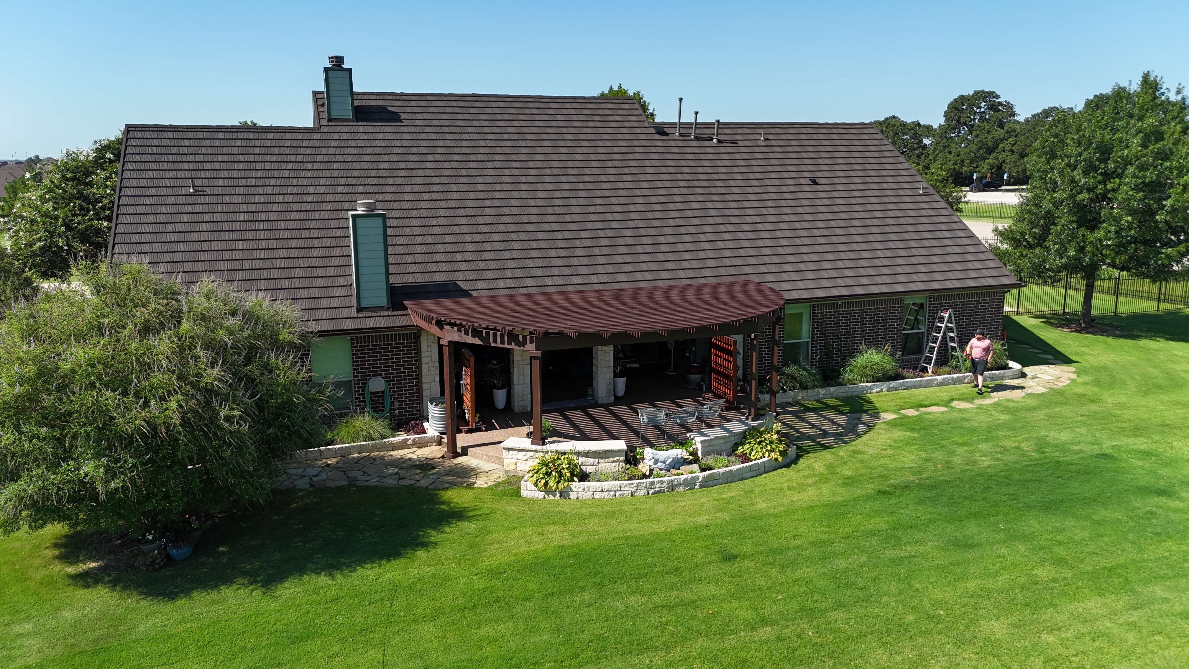 Rear view of brown stone coated steel roof over brick home with pergola patio