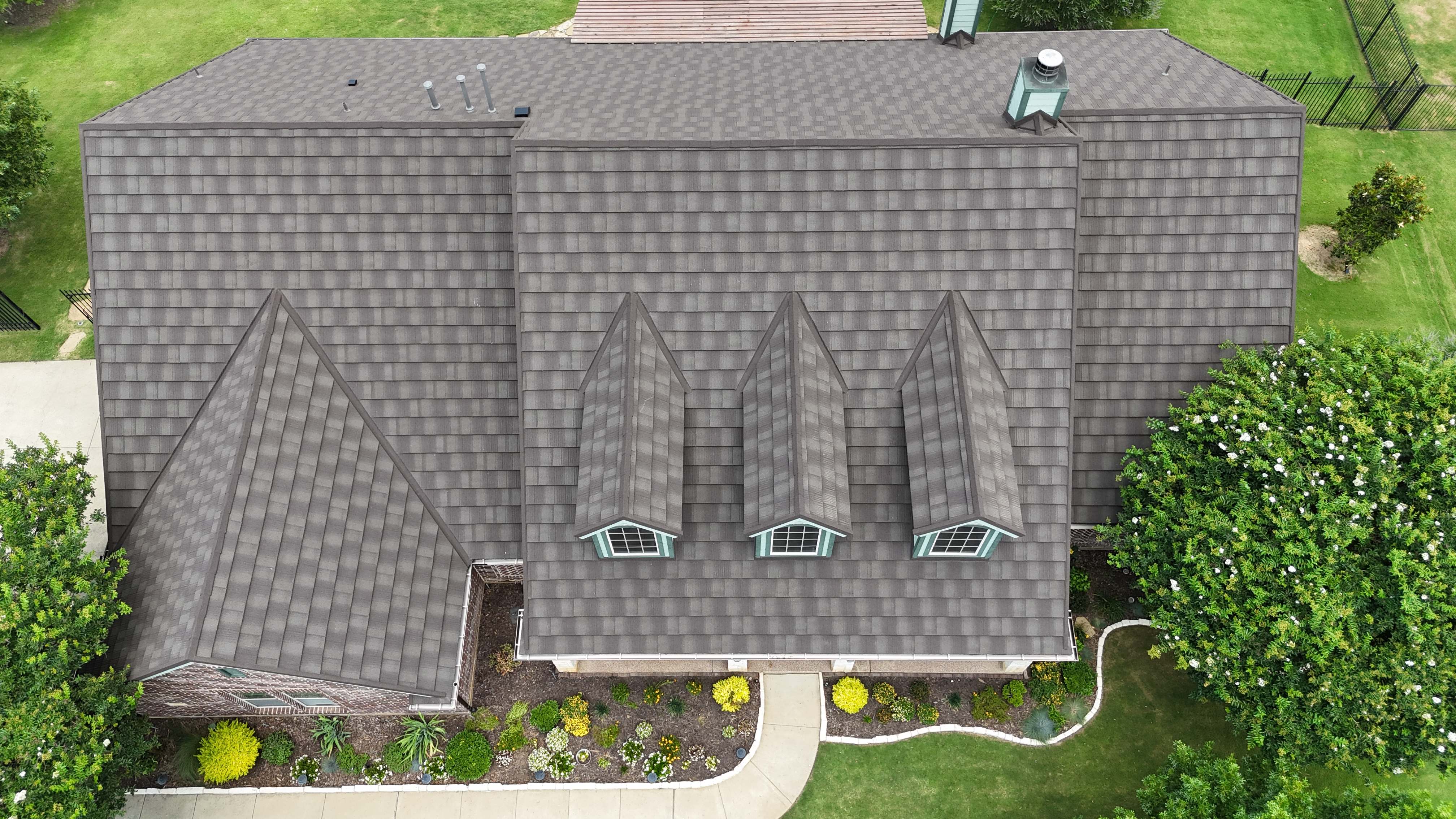 Top-down aerial of brown stone coated steel shingle roof with three dormers