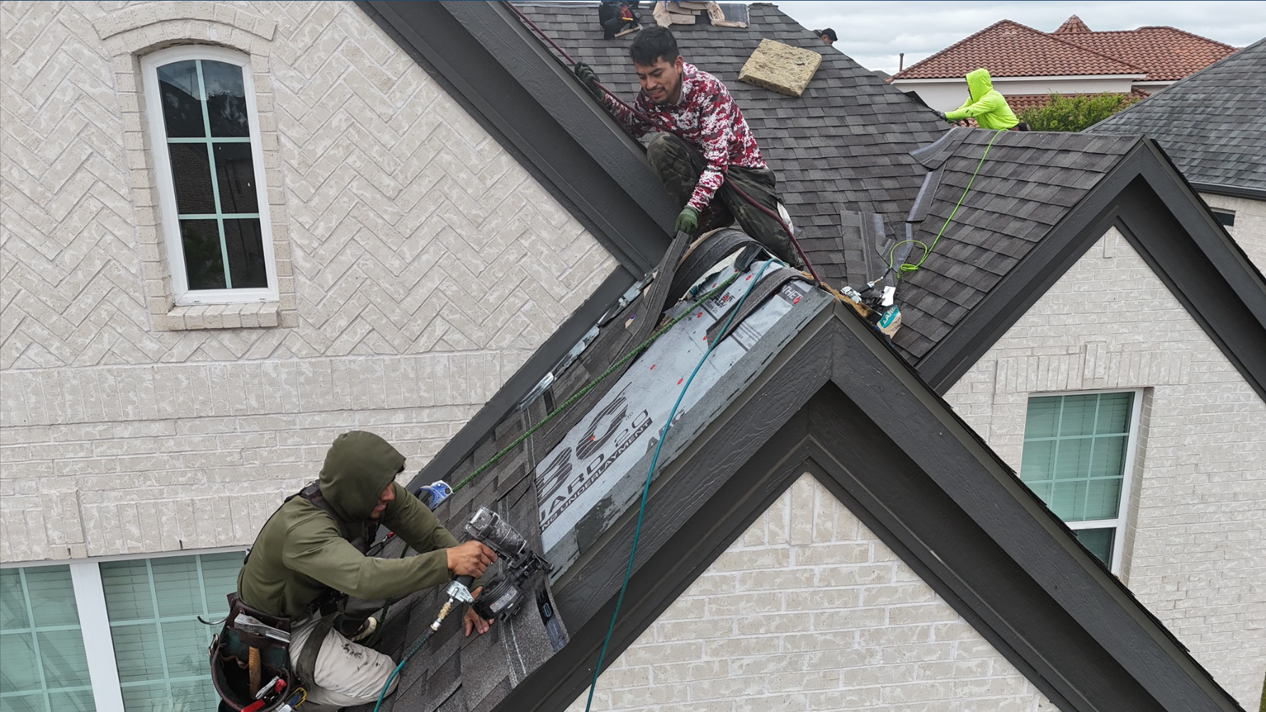 Crew members installing ridge cap shingles at roof peak