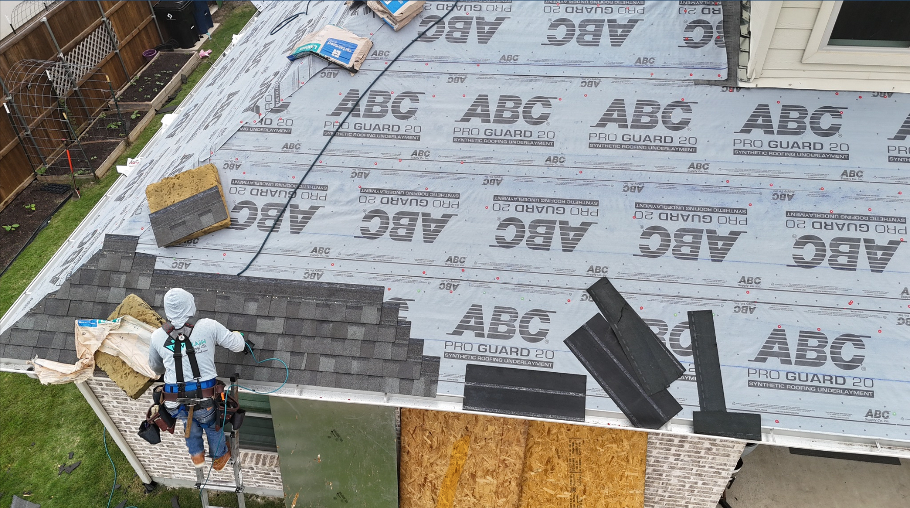 Roofer with safety harness installing shingles professionally