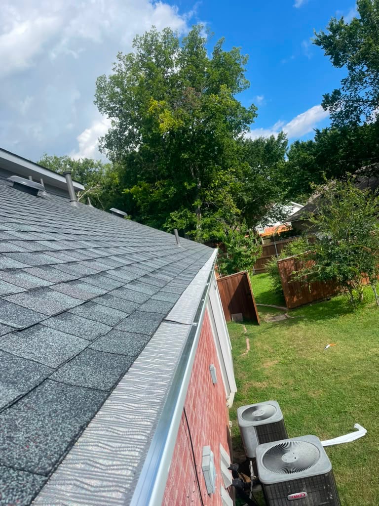 Roof edge with new gray shingles and gutter against blue sky