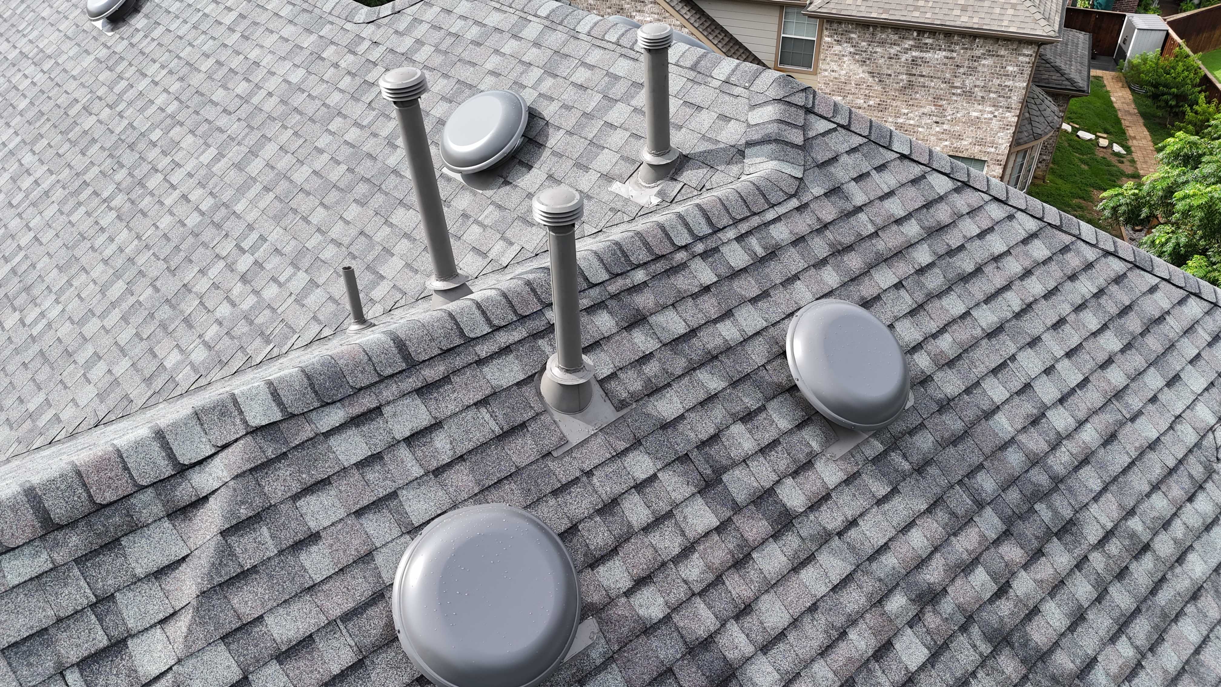 Detailed view of gray shingle roof with multiple vents and pipe collars