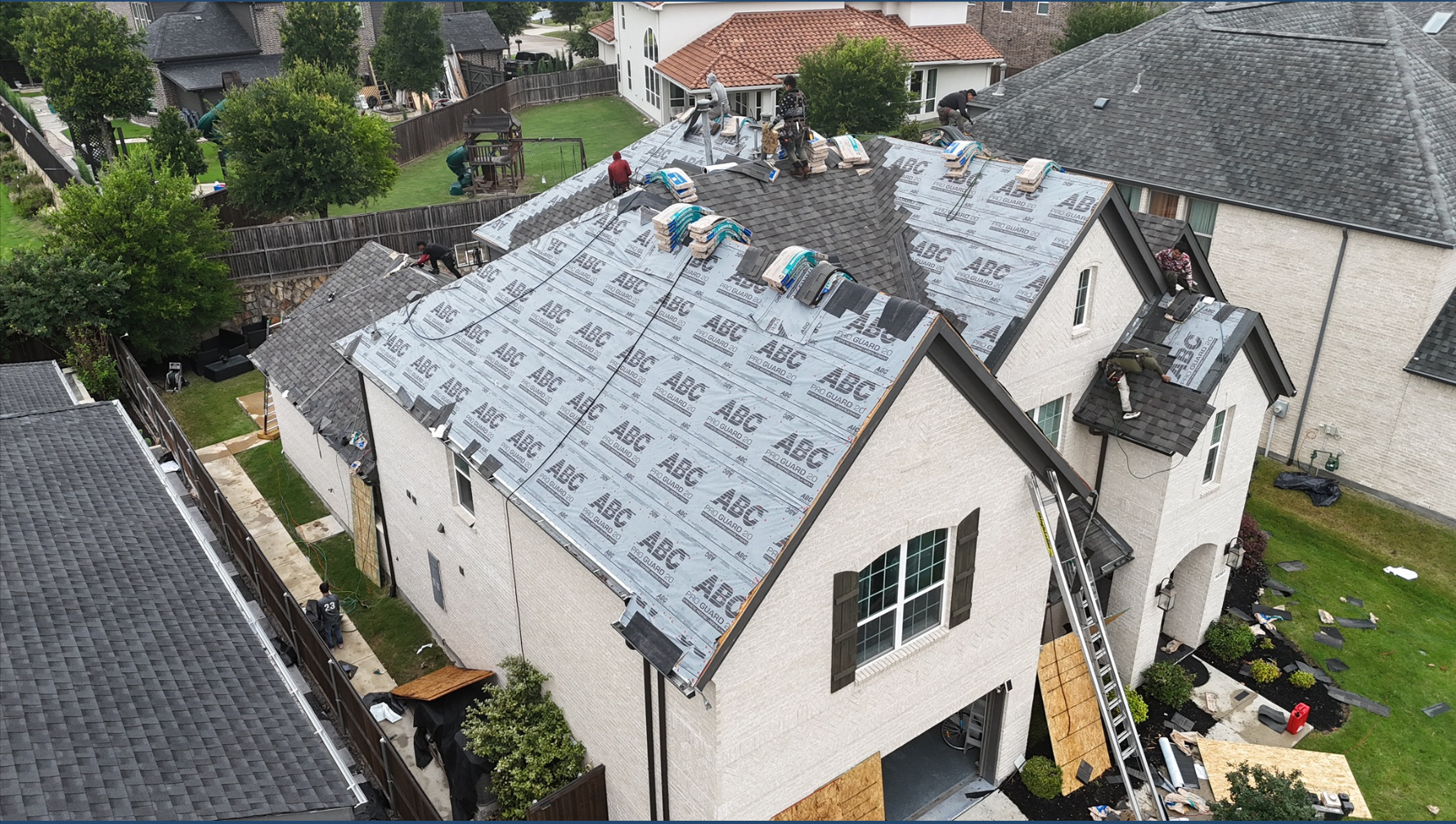 Large white stucco home with underlayment and shingle installation